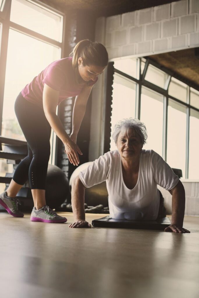 Trainer assisting older woman exercising.